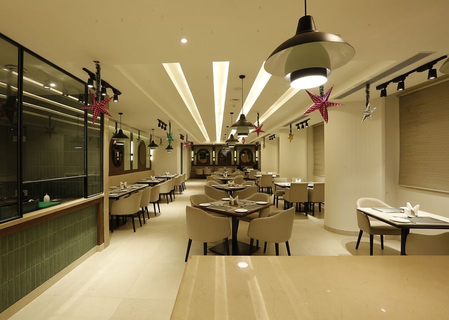 An image of a restaurant with several sets of table and chairs, lights installed on the ceiling, stars hanging from the ceiling, and there is also a counter at one side of the room - Tulip Inn, Zirakpur