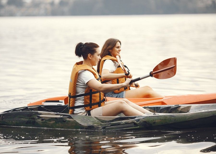 Two women in life jackets kayaking on a calm lake, surrounded by serene water and lush greenery.
