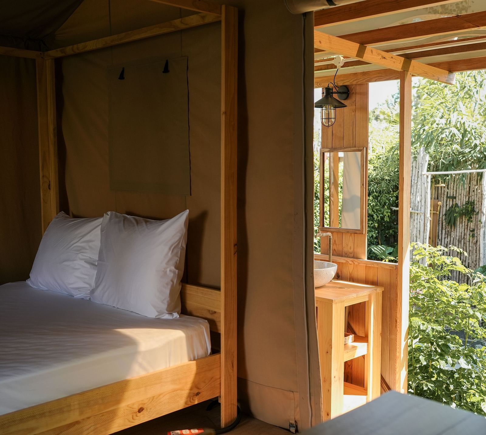 A serene bedroom inside the Mindful Tent at WoCAL Retreat Ke Ga, highlighting a cozy bed with white linens, wooden furnishings, and a window view of lush greenery outside.