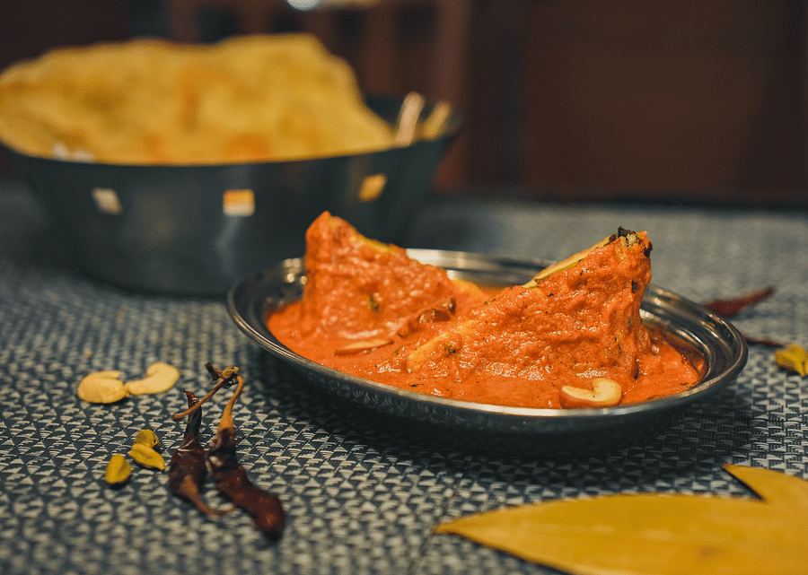 A serving of curry on a steel plate, accompanied by roti on another plate, with various spices put on the table