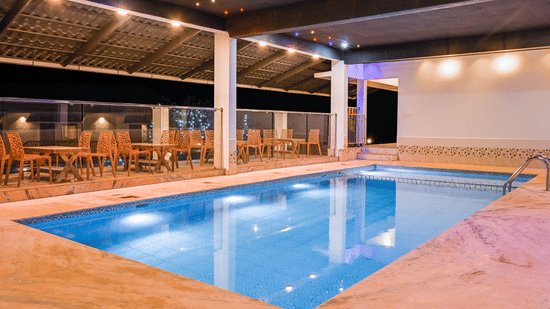 An outdoor swimming pool illuminated at night with several dining tables and chairs arranged on the surrounding deck at Abad Silvermist, Vagamon.