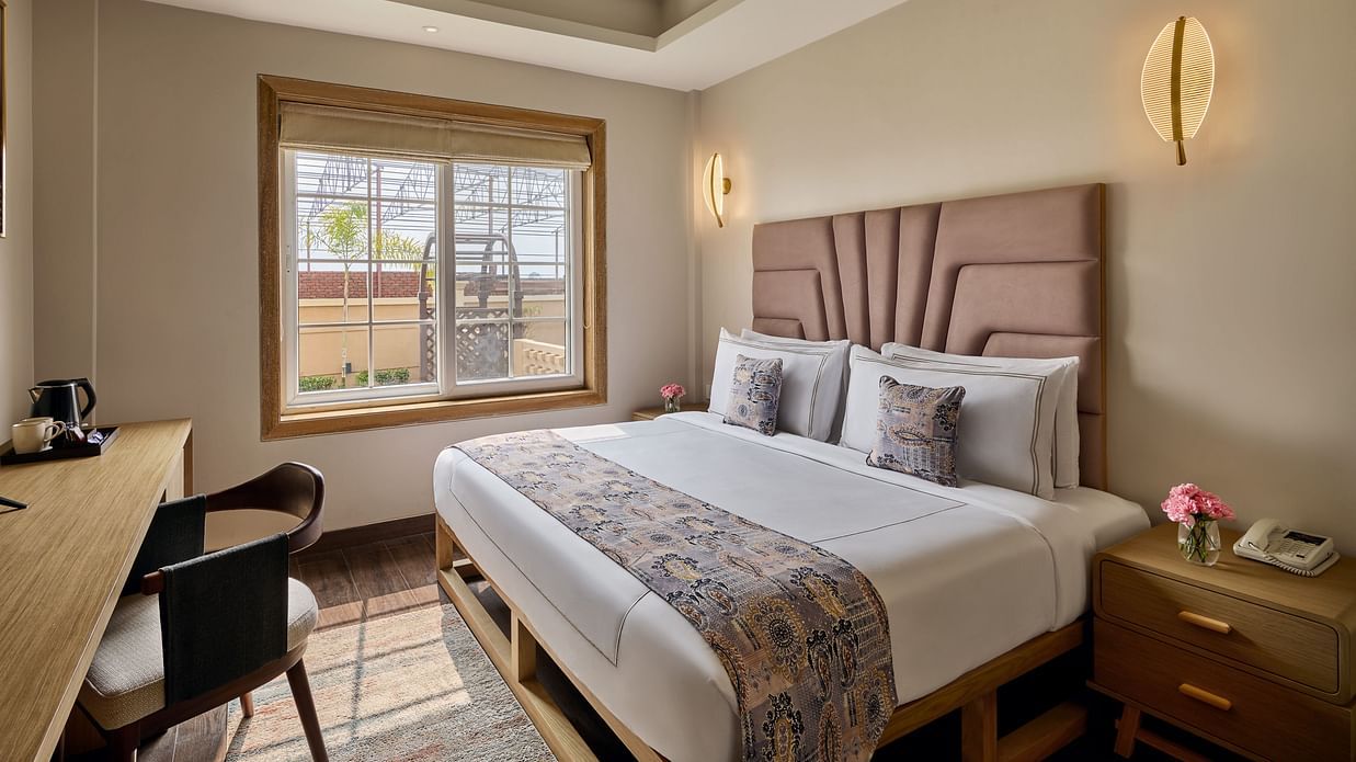 Cosy hotel bedroom with a double bed, padded headboard, wooden desk with a TV, ceiling fan, and a large window letting in natural light - Voyage The Solitaire Bliss.
