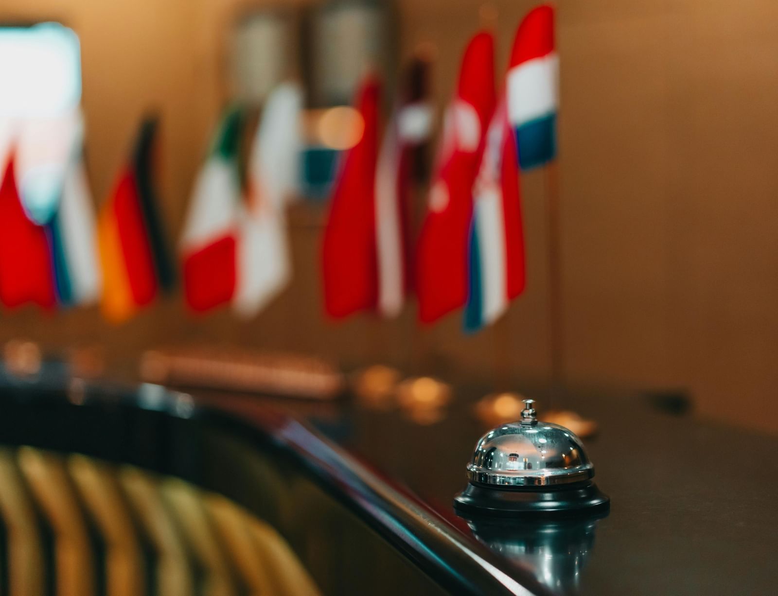 A service bell on a reception desk, with a row of small international flags in the background, symbolising global hospitality and welcoming guests worldwide.