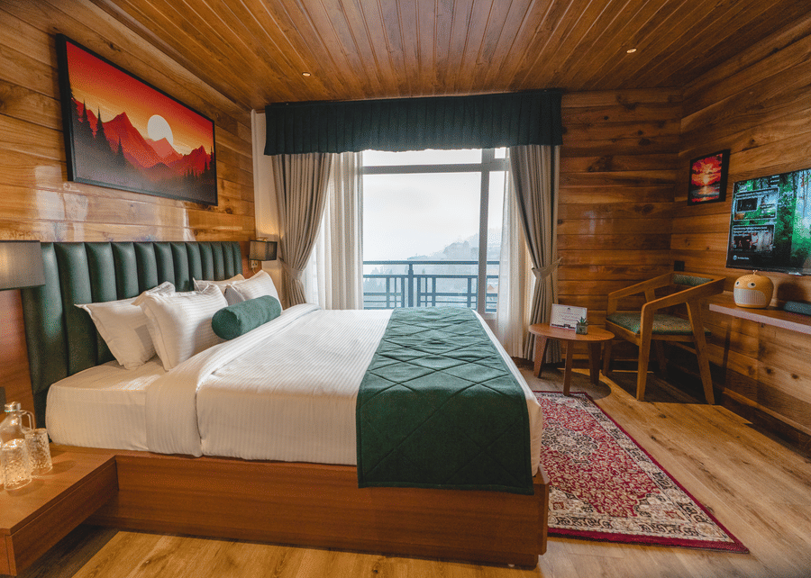 The bedroom of Presidential Suite with Bathtub featuring a double bed with a green bed runner, a wall-mounted television, a seating area and a balcony overlooking the town | Mount Lungta Boutique Hotel & Spa