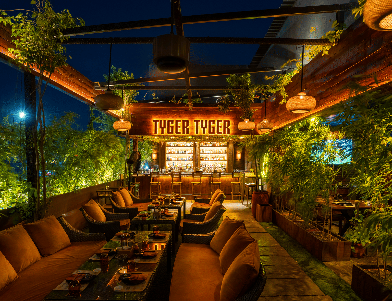 A restaurant seating area with cushioned chairs, tables and a glowing signboard reading 'TYGER TYGER' at Infiniti Hotel, Indore.