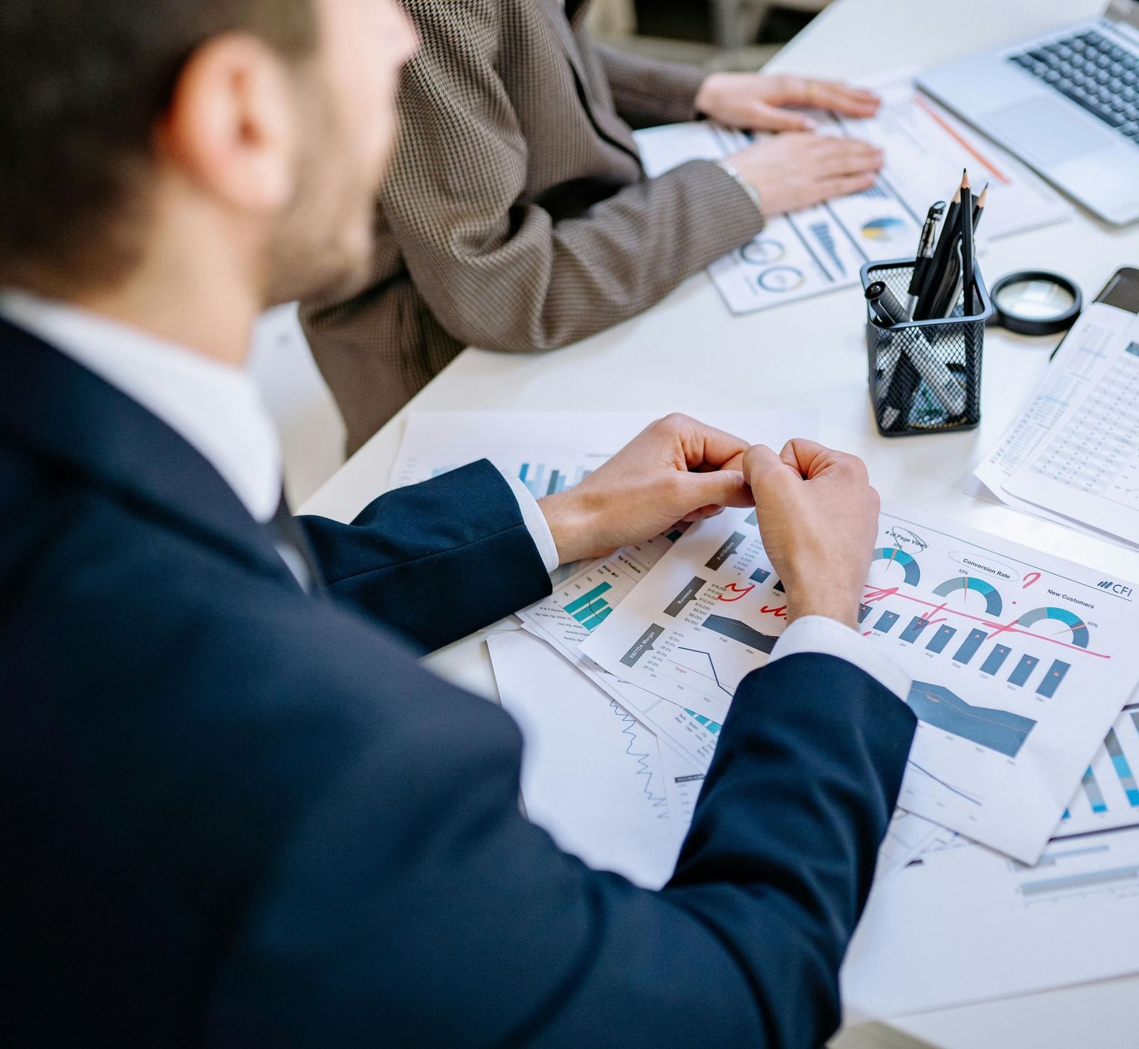 A person dressed in business formals in front of a table with sheets full of data scattered over it.