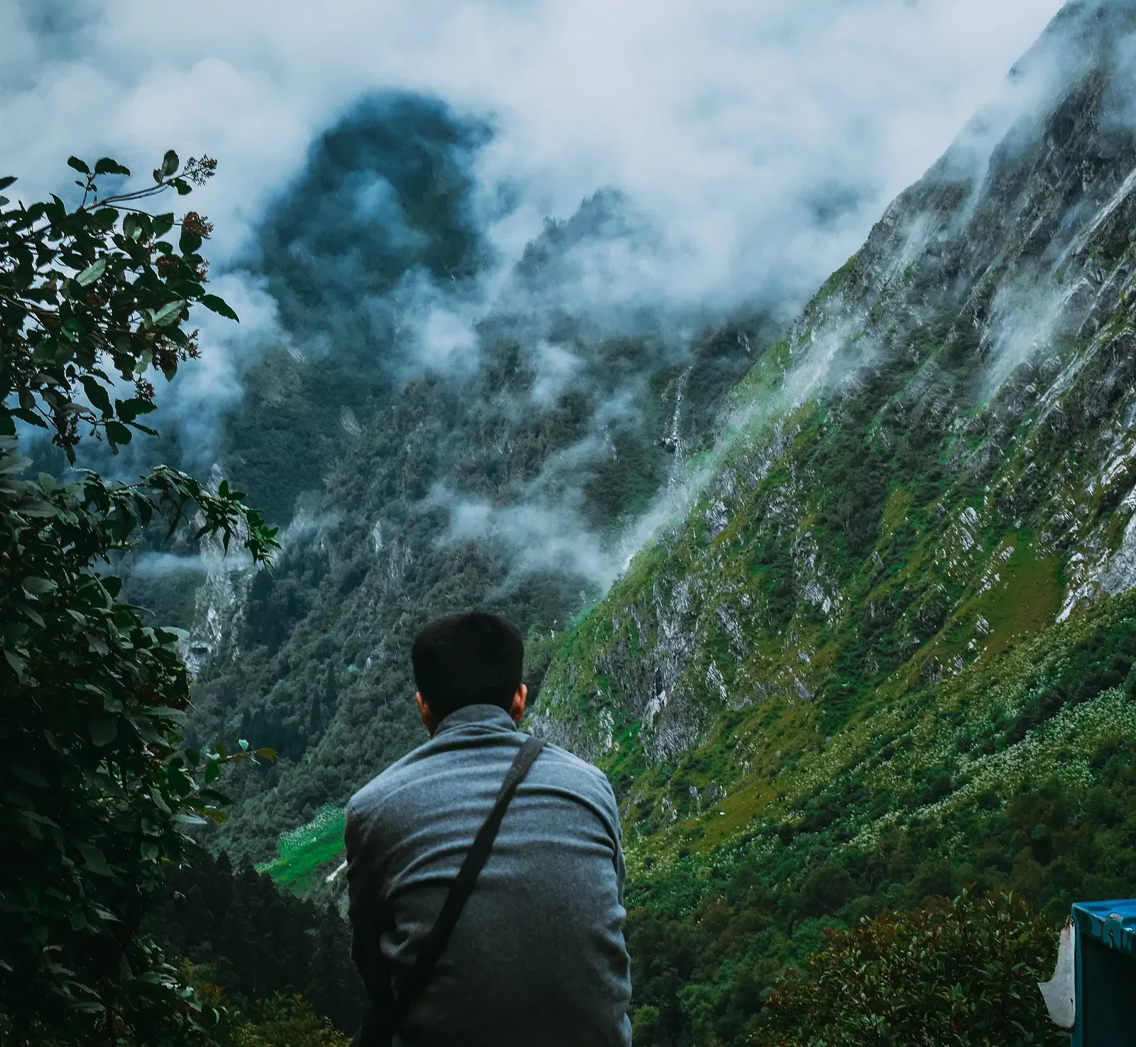A man sits with his back to the viewer, facing a misty mountain valley landscape, with a tent visible in the foreground.