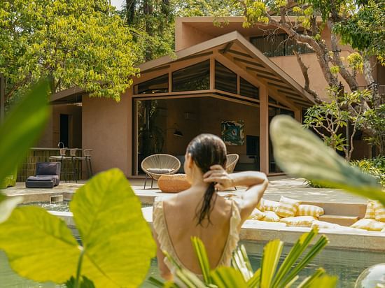 A silhouette of a woman in the swimming pool surrounded by lush green plants along with an outdoor seating area by the pool in the background at Villa Moira by V Escapes.