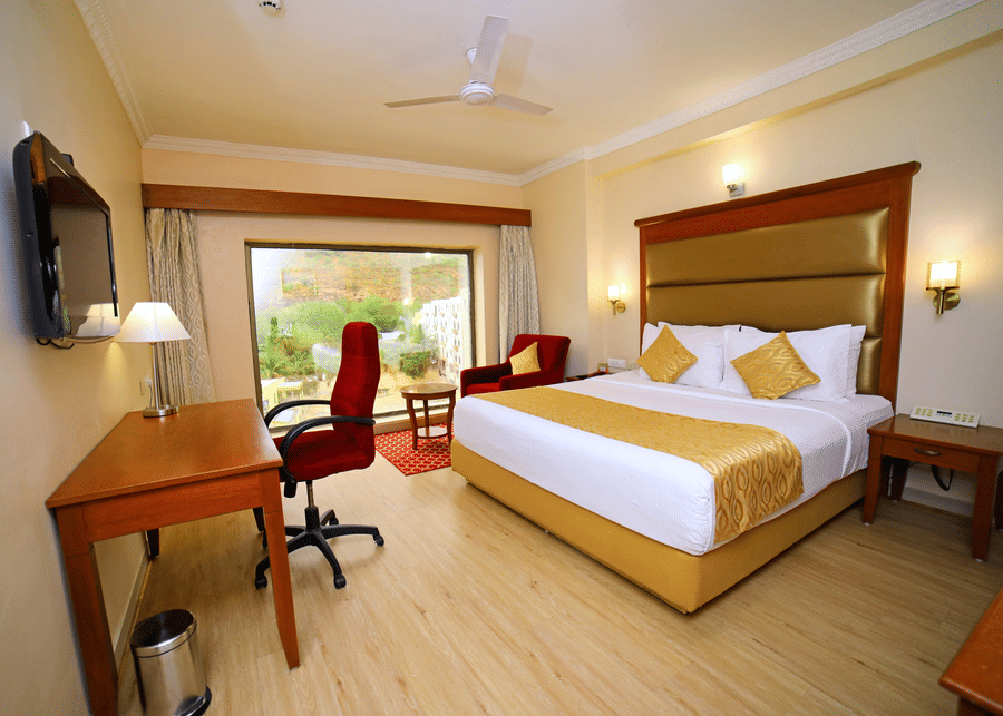 Hill View Room featuring a double bed facing a TV with a lamp on the work desk below, and a sofa next to the window at Raj Park Hotel, offering the best place to stay in Tirupati