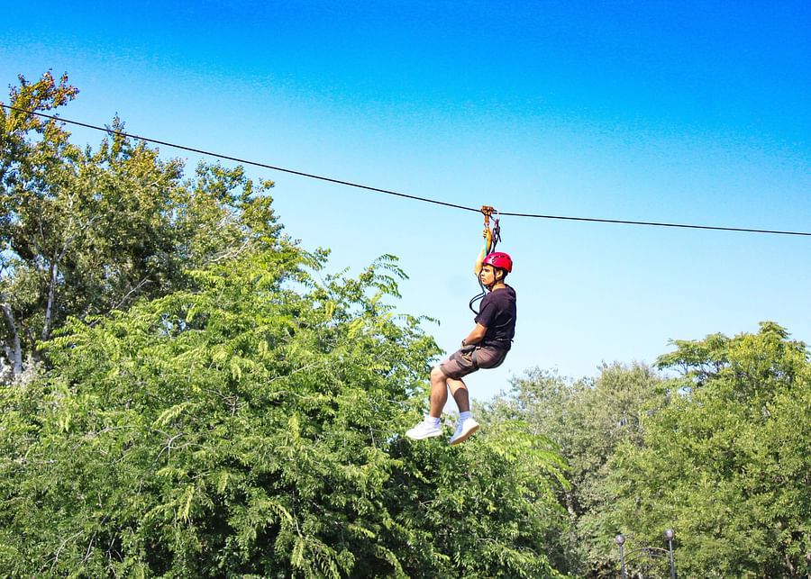 a man on a zip line surrounded by greenery - Adventure Park near Ahmedabad
