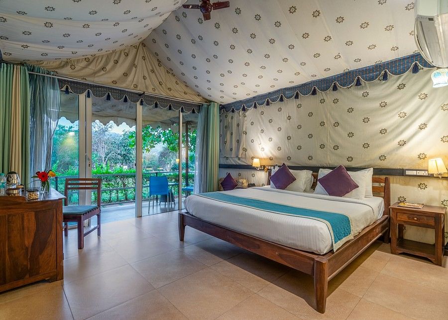 alt-text Glamps Hero - A luxurious bedroom with a canopy ceiling, patterned walls, and a scenic view through large windows.
