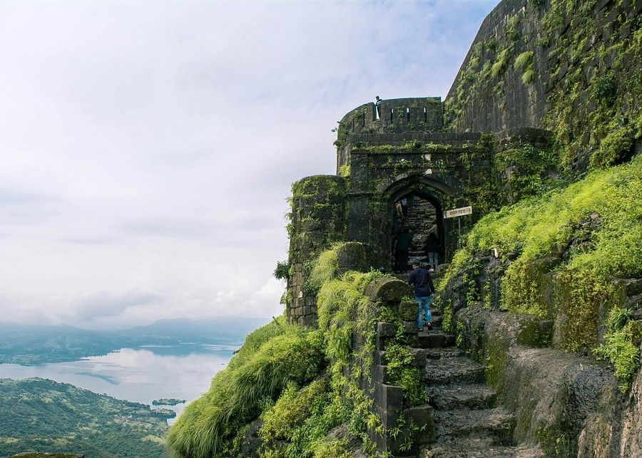 Ancient stone steps and archways covered with green moss on a foggy mountain, evoking a sense of mystery and historical depth in a natural setting.