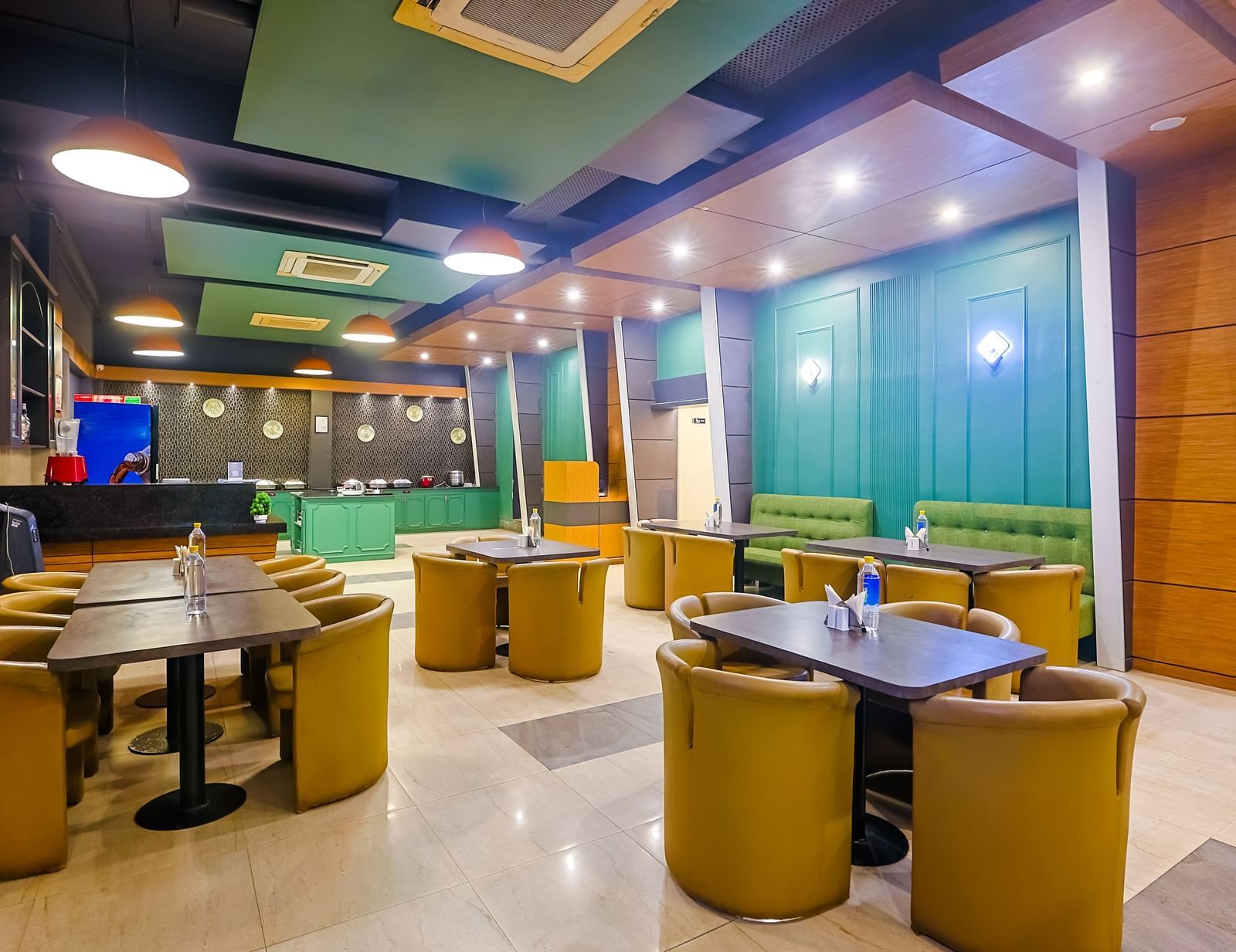 Restaurant dining area with round tables, cushioned chairs and lighting at Max Hotel Prayagraj.