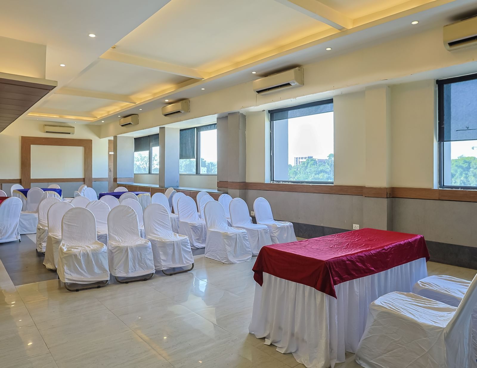Banquet hall with rectangular tables, white chairs and large windows at Max Hotel Prayagraj.