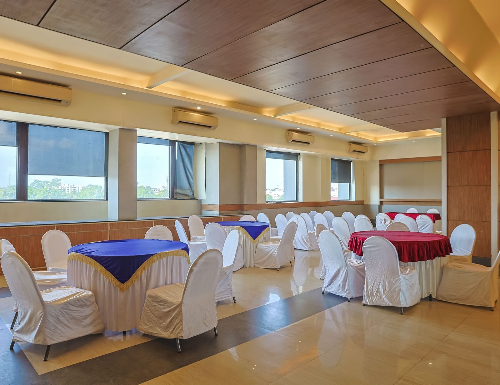 Banquet hall with white chairs, wooden ceiling and bright lighting at Max Hotel Prayagraj.