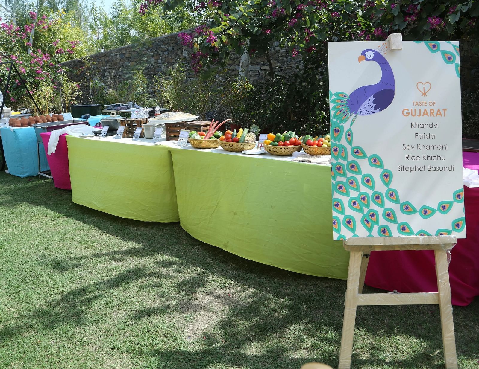 A neatly arranged buffet table with green cloths, peacock sign banner in an outdoor setting.