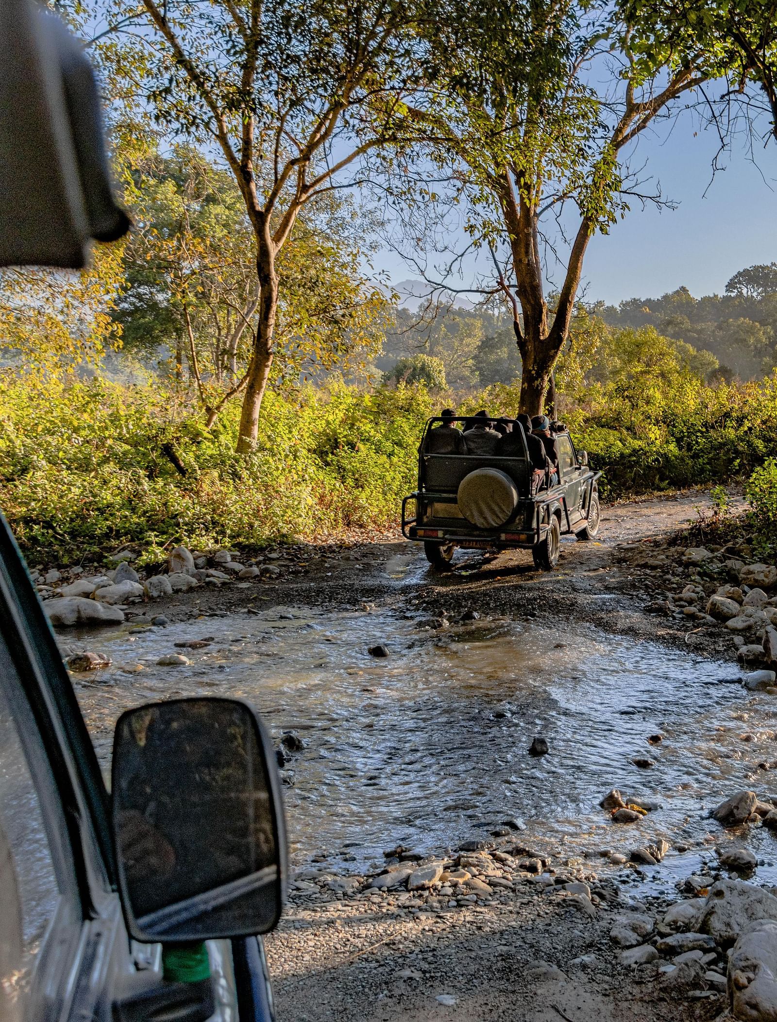 image of two safari jeeps traversing through a stony water stream at Jim Corbett