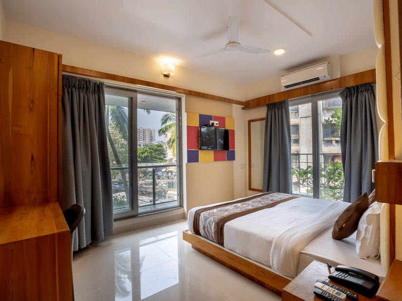 A bedroom with a double bed with 2 big french windows allowing natural light to flow into the room at Home2 Suites & Service Apartments, Mumbai Airport.