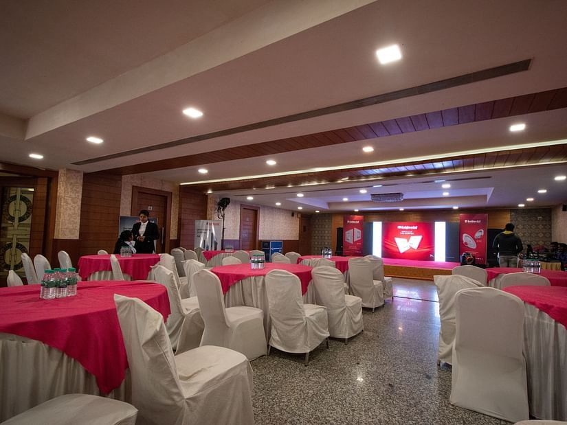 The spacious interiors of the Banquet features chairs draped in white and white & red tables - Wedlock Greens Hotel Resorts Dhanbad