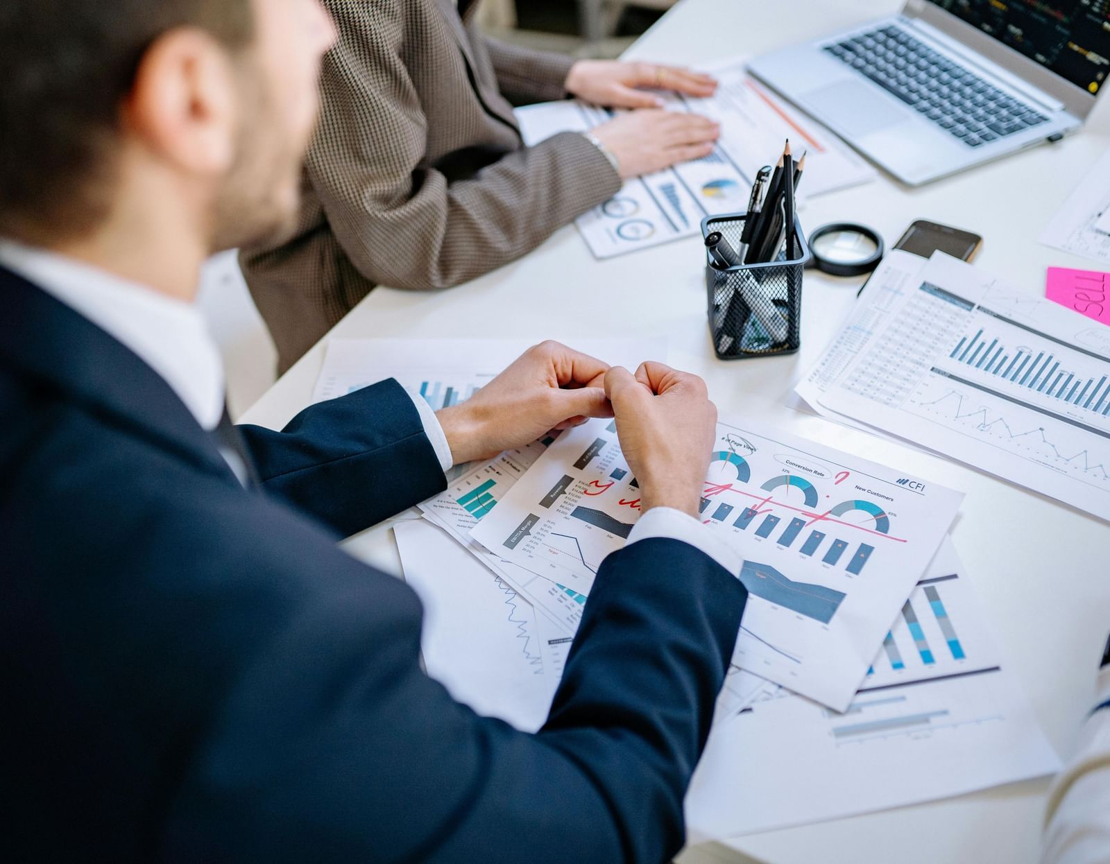 A person dressed in business formals in front of a table with sheets full of data scattered over it.