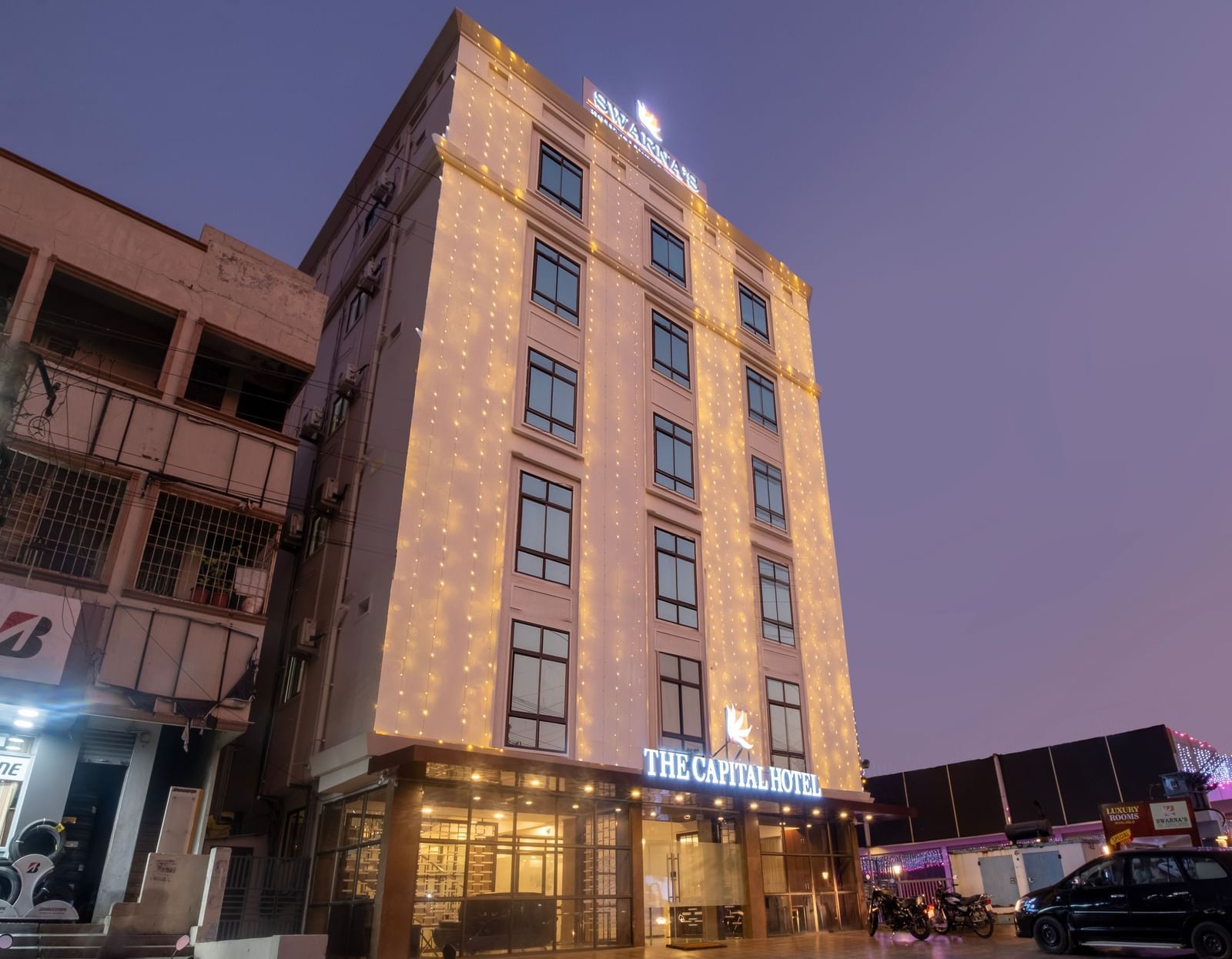 Evening exterior view of Swarna's The Capital with illuminated facade and welcoming entrance.