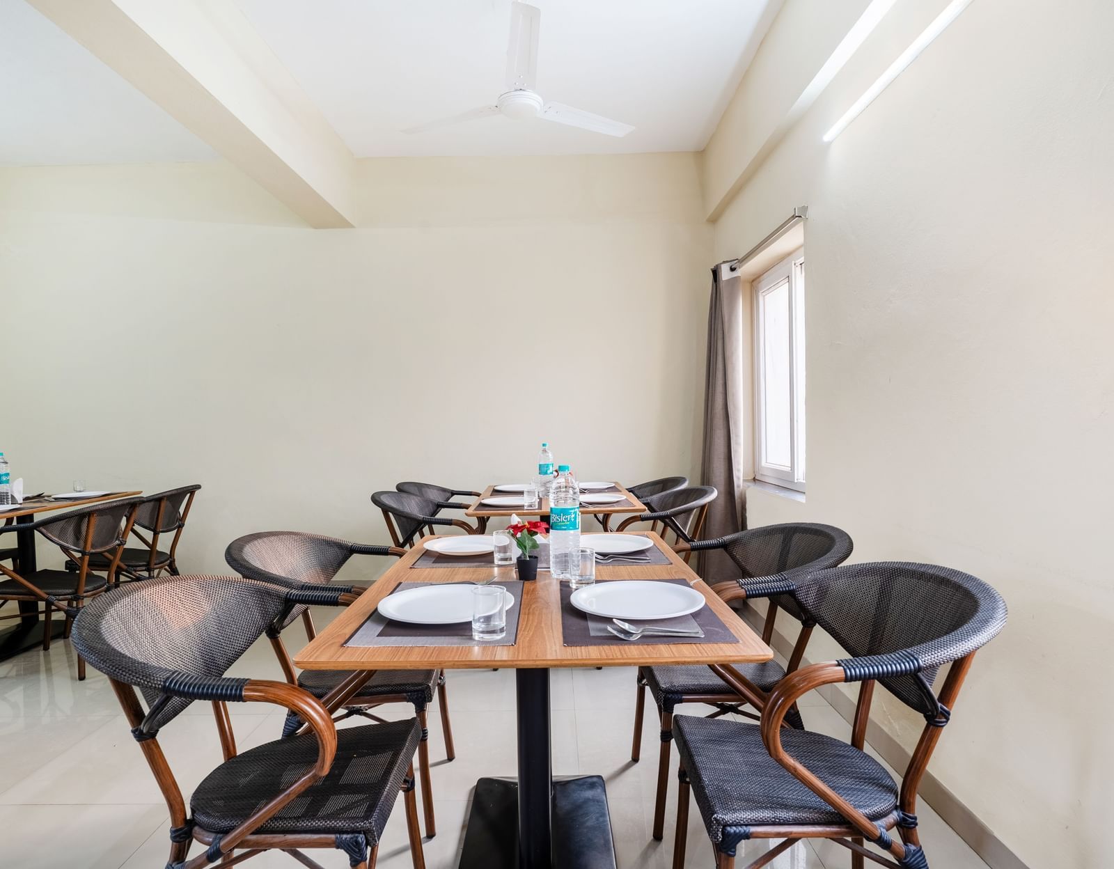 An empty dining area at Destino by Monday Hotels, Gachibowli, with 2 dining tables and woven chairs, set up with plates and water bottles.