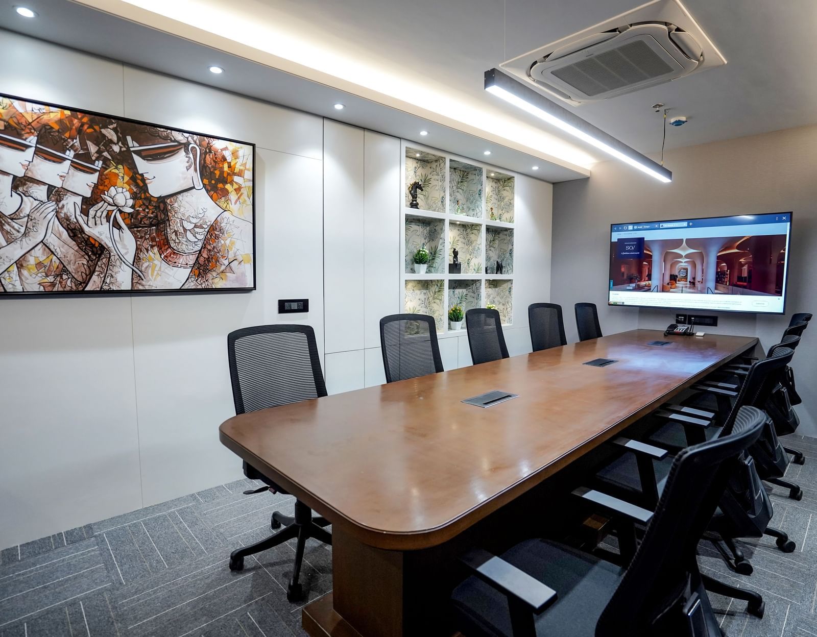 The boardroom at M2 Square by Monday Premium featuring a long wooden table along with an abstract painting hung on the wall.