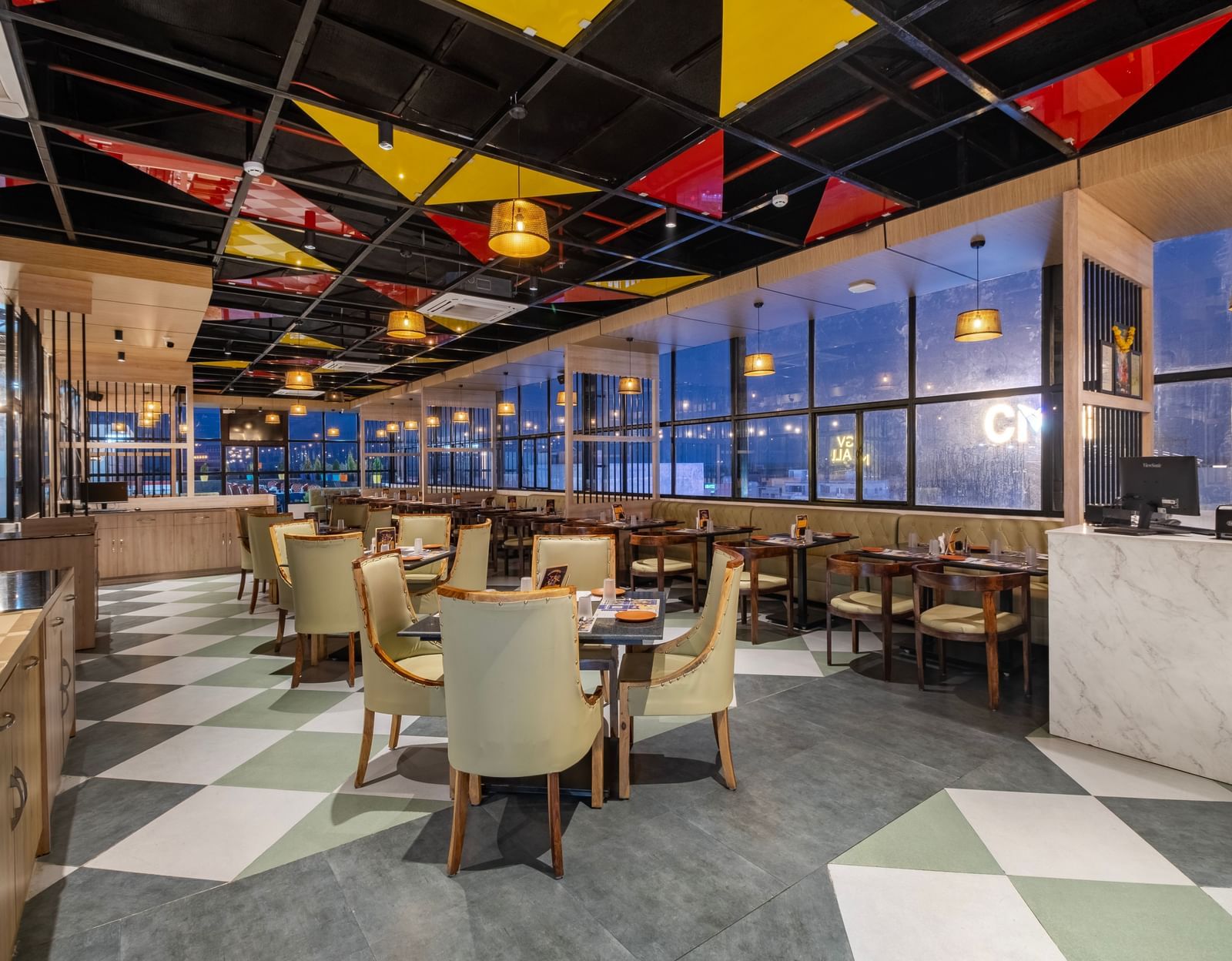 Restaurant at Monday Hotels Amalapuram Heights with colourful ceiling decor, city view, and neatly arranged tables and chair.