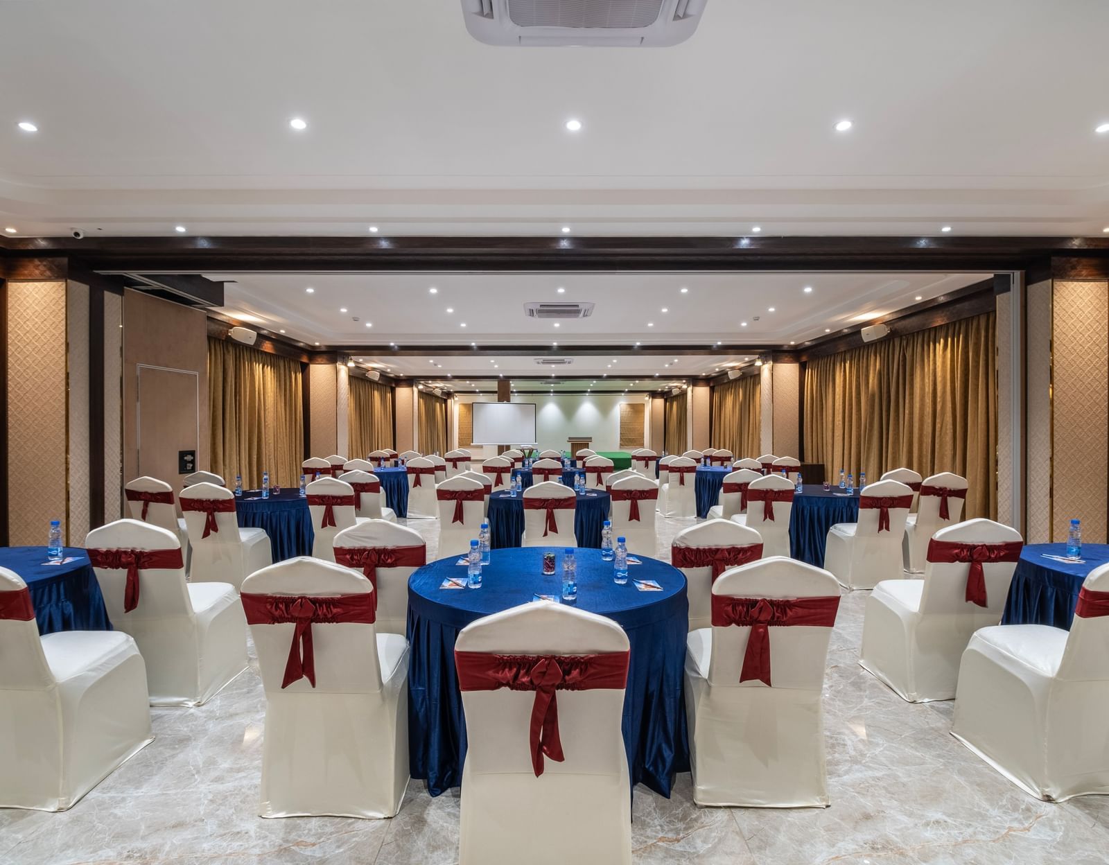 Back view of an event space at Monday Hotels Amalapuram Heights decorated with covered chairs.