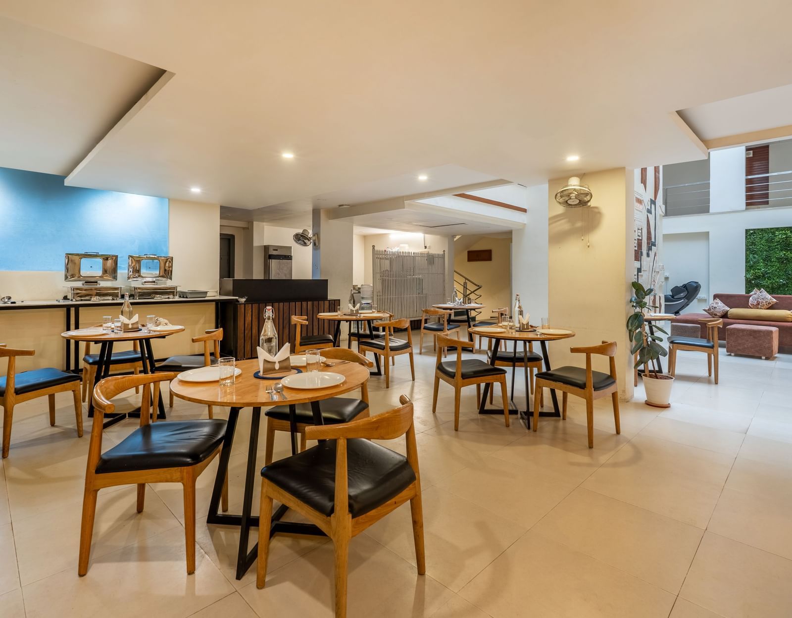 A large dining space with wooden tables, chairs, and an open kitchen view - Monday Hotels HITEC City, Hyderabad