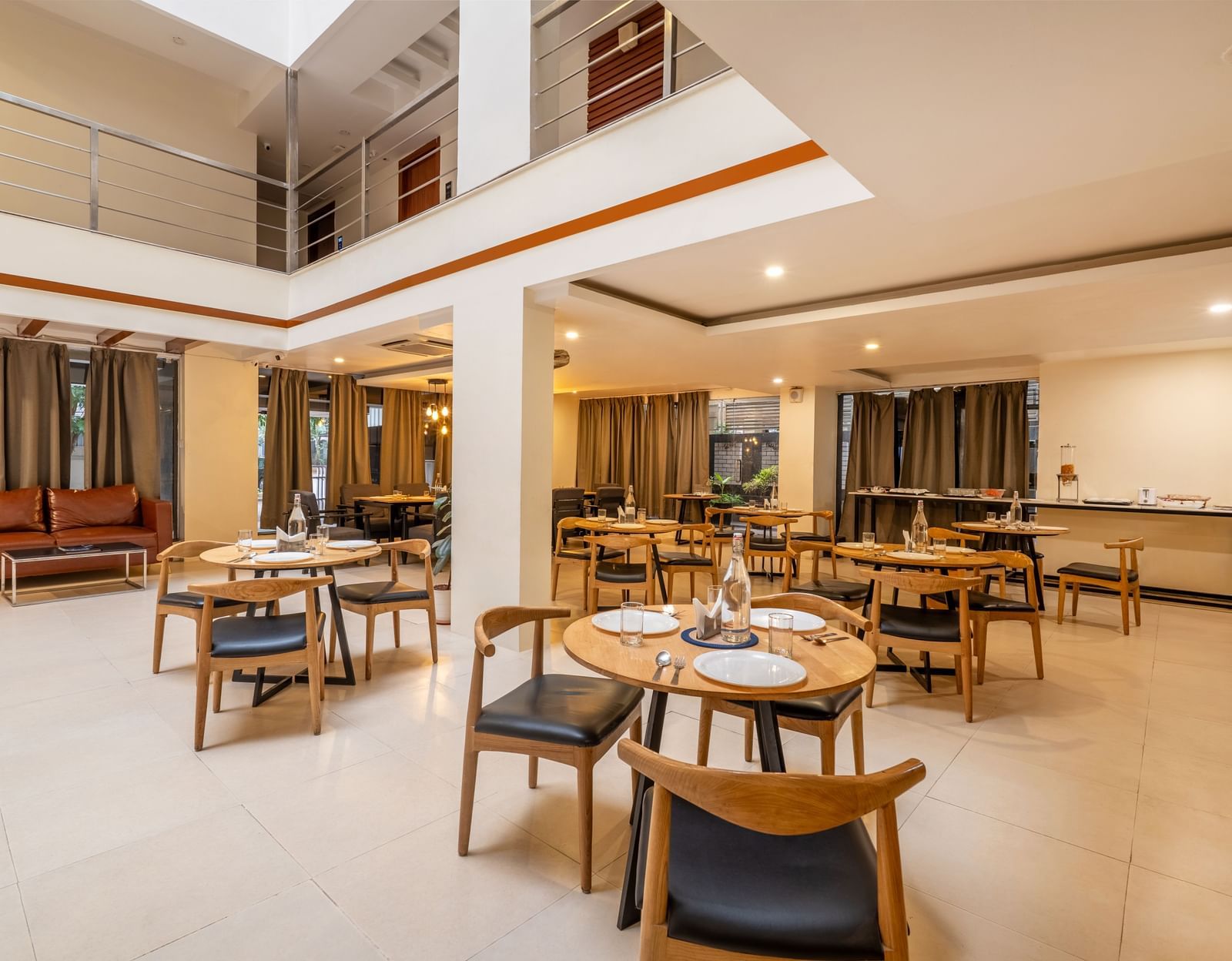 A dining area with multiple tables and chairs arranged neatly and a seating area with a cushioned sofa - Monday Hotels HITEC City, Hyderabad