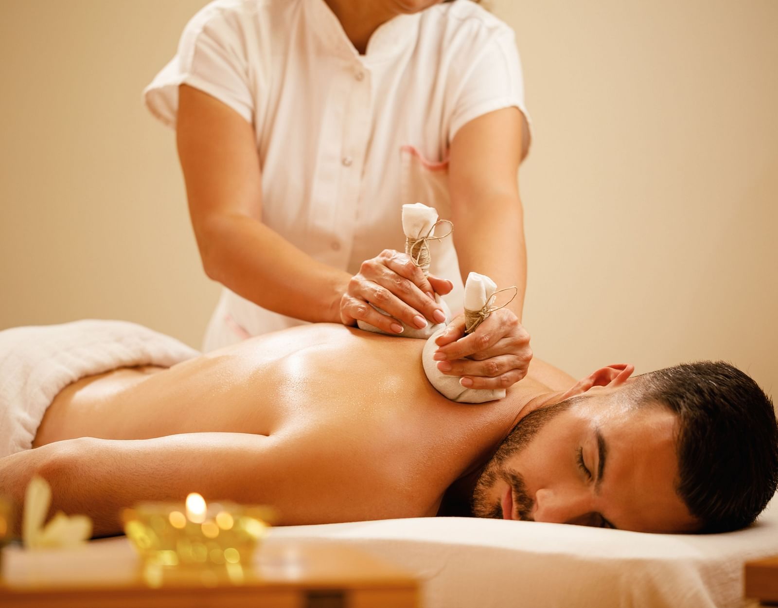 Woman using herbal pouches to massage a man's back.