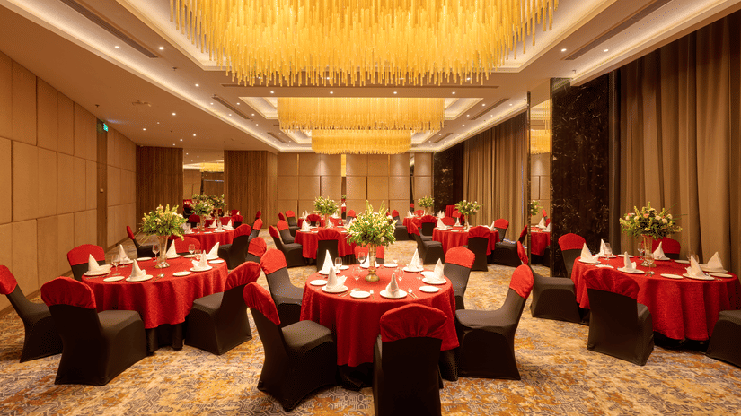 A large banquet hall at KPG Sarovar Portico, Raj Nagar Extension, Ghaziabad featuring round dining tables, chairs, chandeliers, and carpeted flooring.
