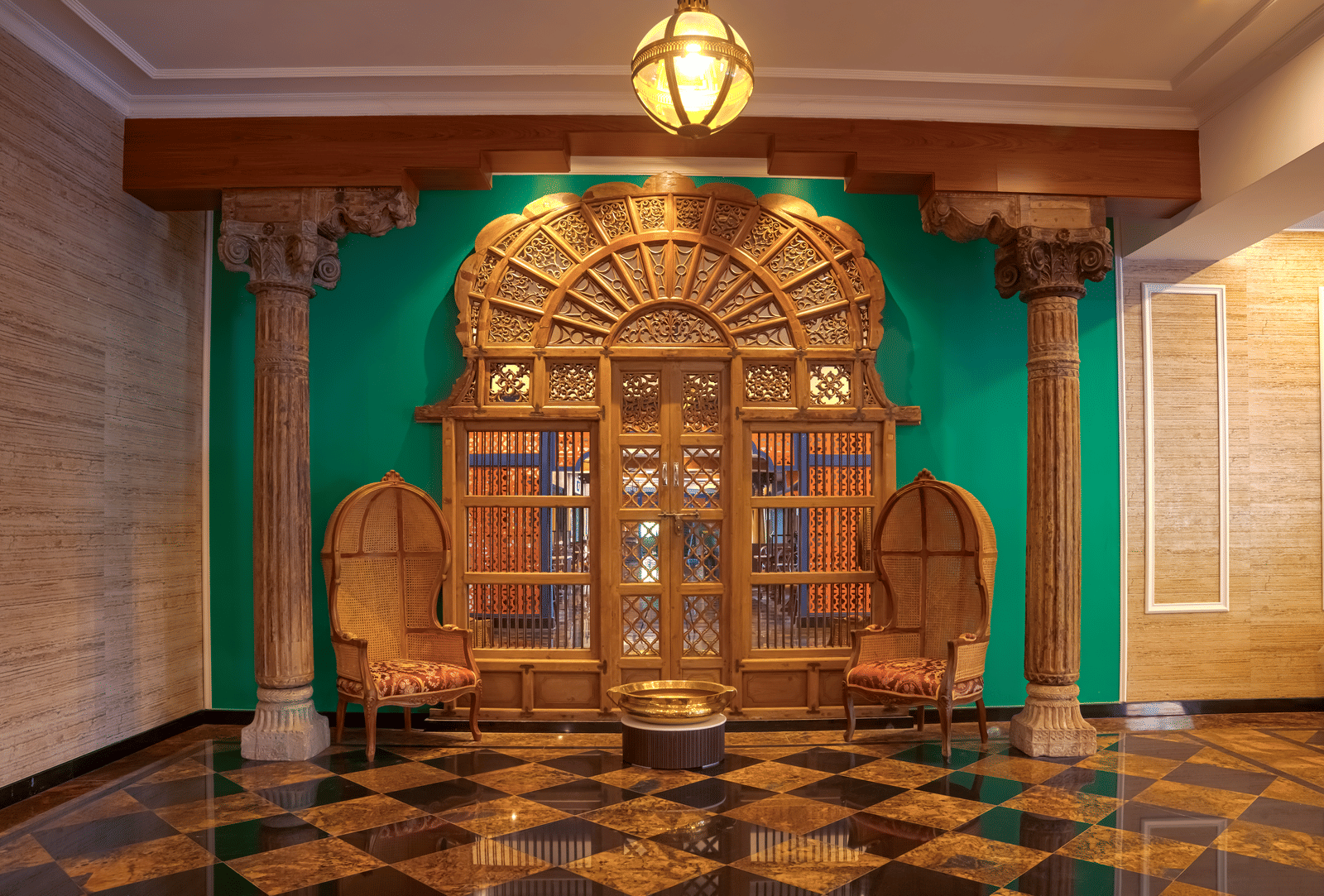 A richly designed corridor featuring carved wooden doors, ornamental seating, polished tiled flooring, green wall accents and overhead lantern lighting at MAYFAIR Bay Resort, Paradeep.