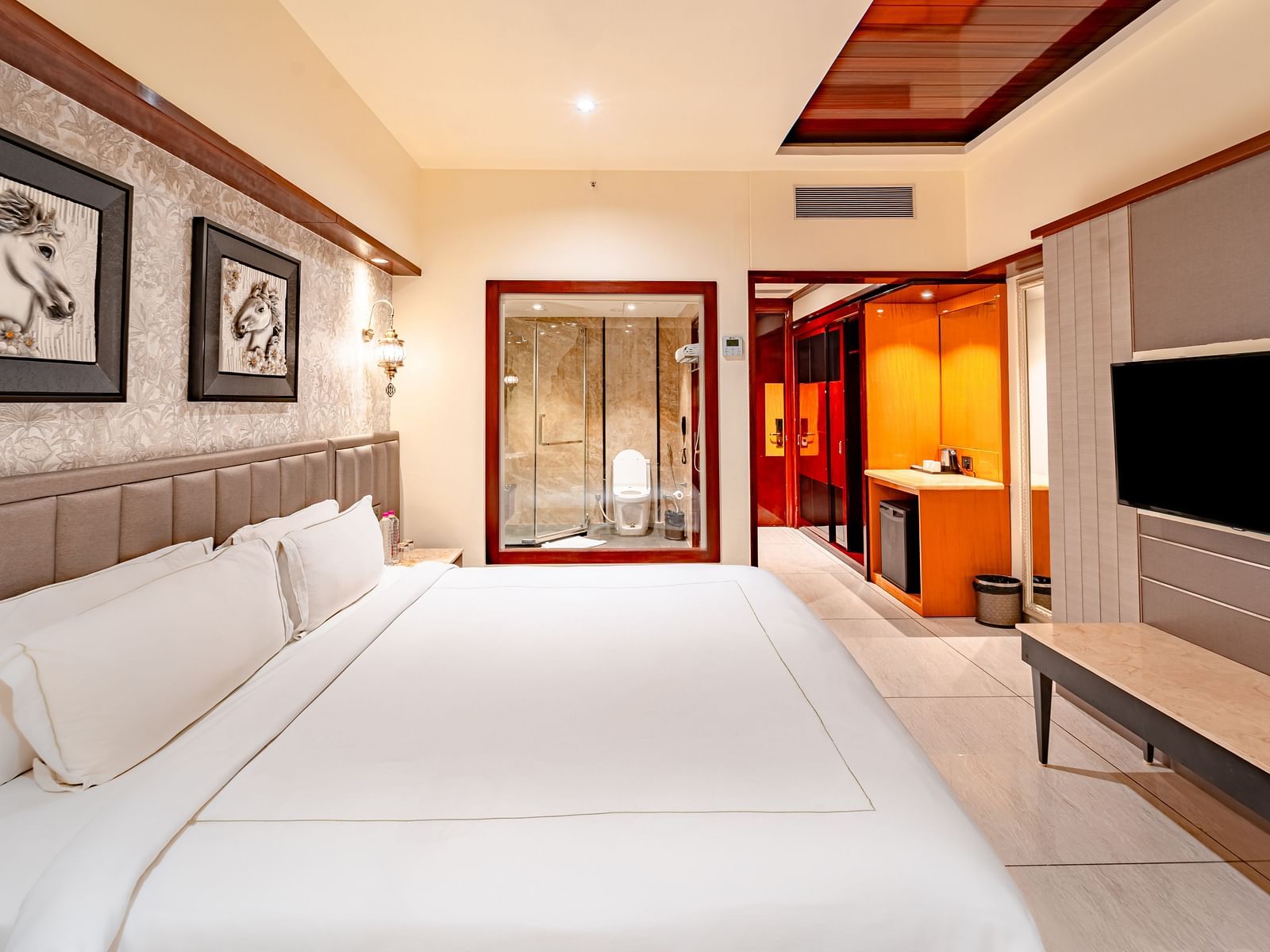 Deluxe Room side view features a spacious bed with a wall-mounted television directly opposite, two photo frames above the headboard at Crescent Spa & Resort, Indore