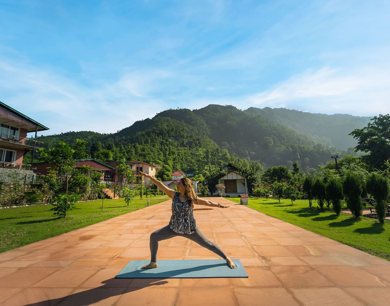 a woman doing yoga in an open area with a mountain in the background - Neer Ganga Resorts