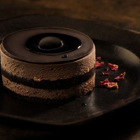 Dark chocolate mousse cake with a glossy top and petals.