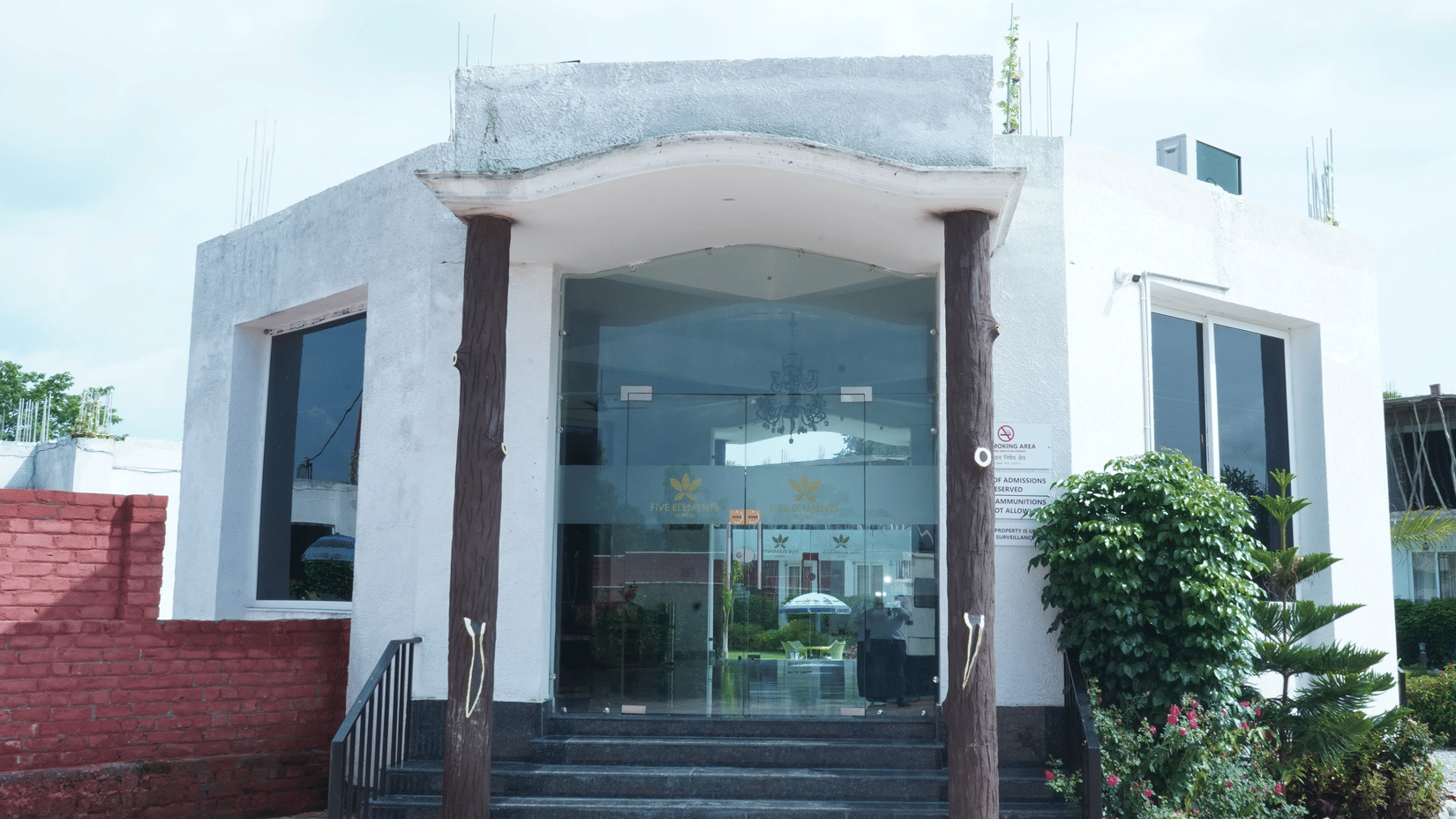 Exterior front entrance view of the hotel main building featuring large glass doors, steps, and surrounding landscape - Five Elements Hotels, Corbett Crown Resort, Jim Corbett