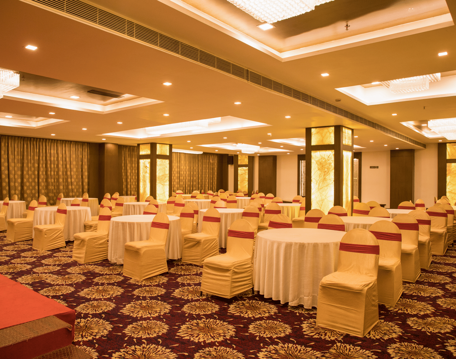 A spacious banquet hall at Benzz Park Chennai with numerous round tables draped in white, set for a gathering.