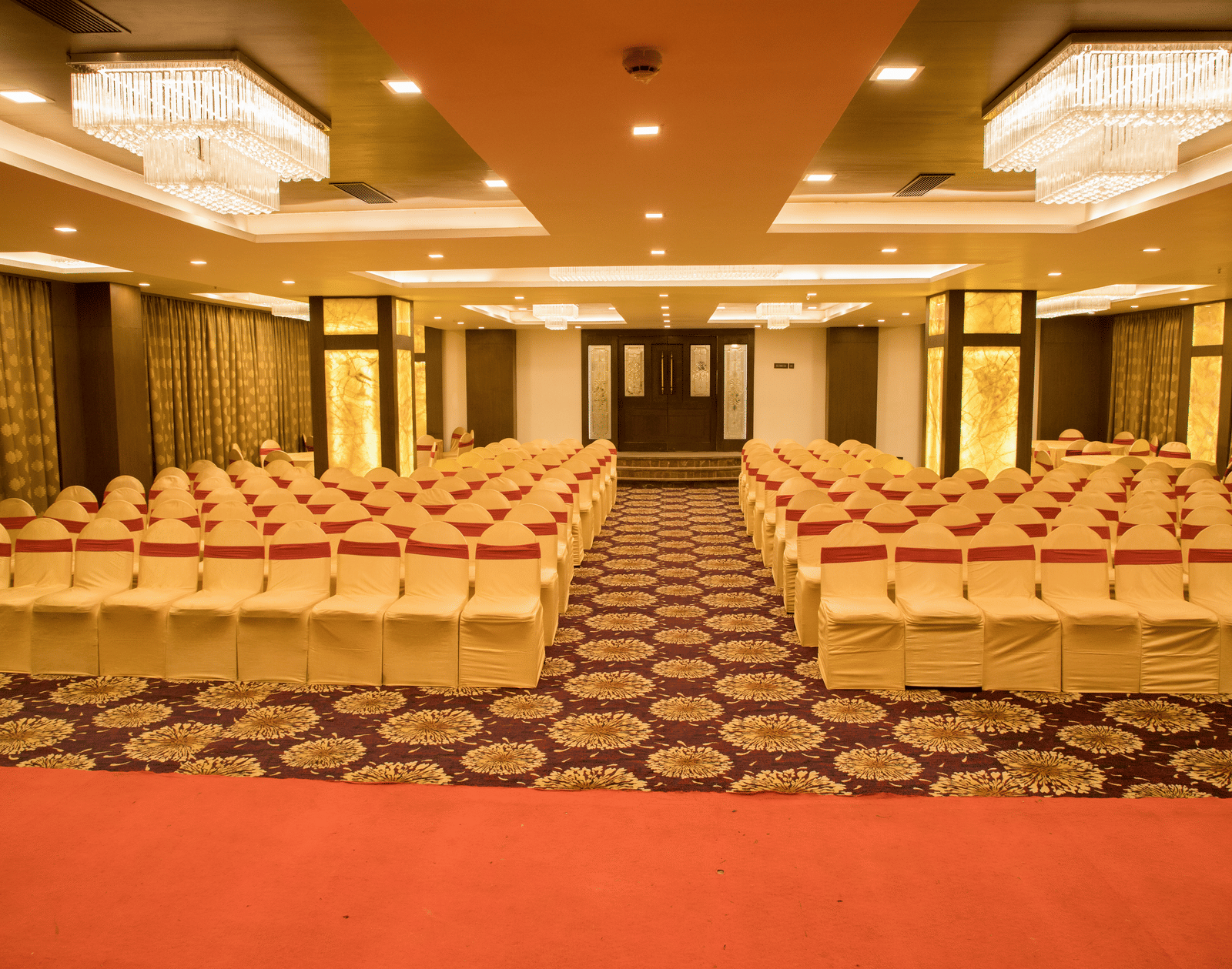 A banquet hall at Benzz Park Chennai arranged with numerous chairs in rows, featuring a patterned carpet and warm lighting.