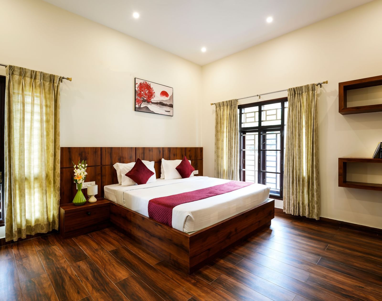  A spacious deluxe room at Bhuthanakadu Retreat, featuring a large bed with a rich wooden headboard, a red and white duvet, and warm recessed lighting.