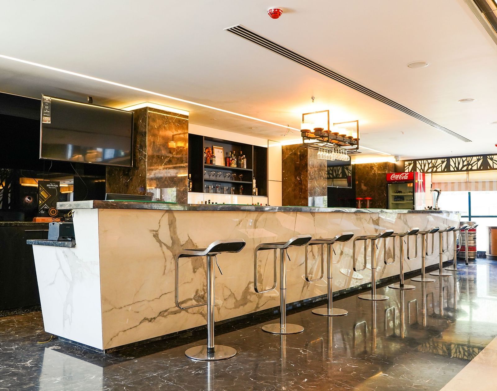 A sleek and modern bar area at BNGV Grandeur Hotel and Banquets, featuring a long counter with multiple high stools and elegant lighting.