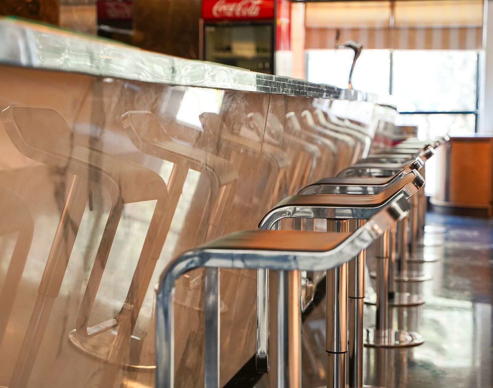 A detailed close-up of a warm-toned wooden bar counter with several bar stools at BNGV Grandeur Hotel and Banquets, highlighting the texture and design.