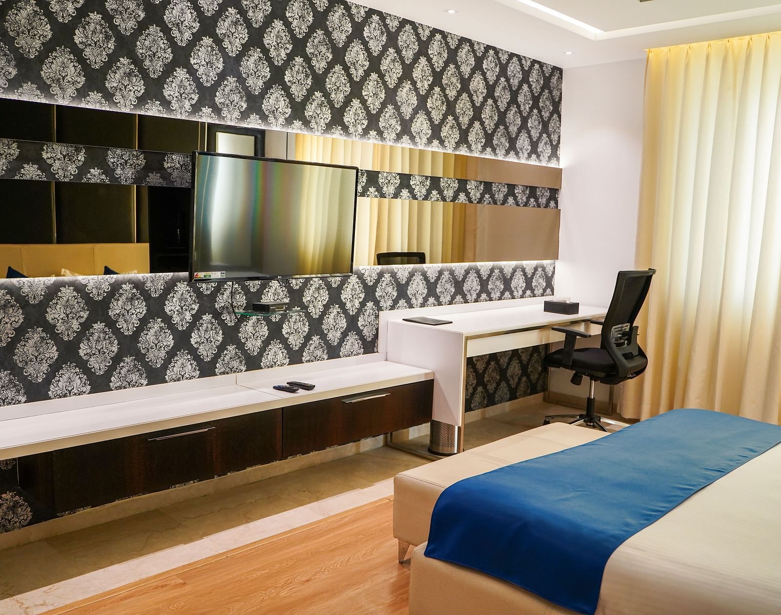A functional and aesthetically pleasing hotel room at BNGV Grandeur Hotel and Banquets, featuring a comfortable bed, a desk with a chair, and elegant decor.
