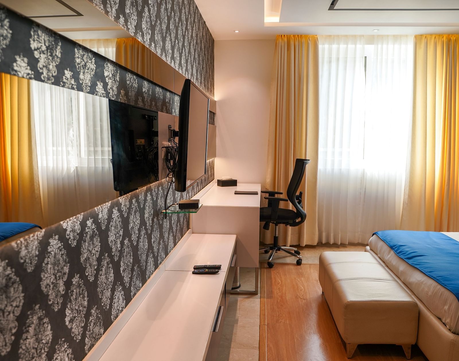 A well-appointed hotel room at BNGV Grandeur Hotel and Banquets, showcasing a bed, a patterned accent wall, a dresser, and a flat-screen TV.