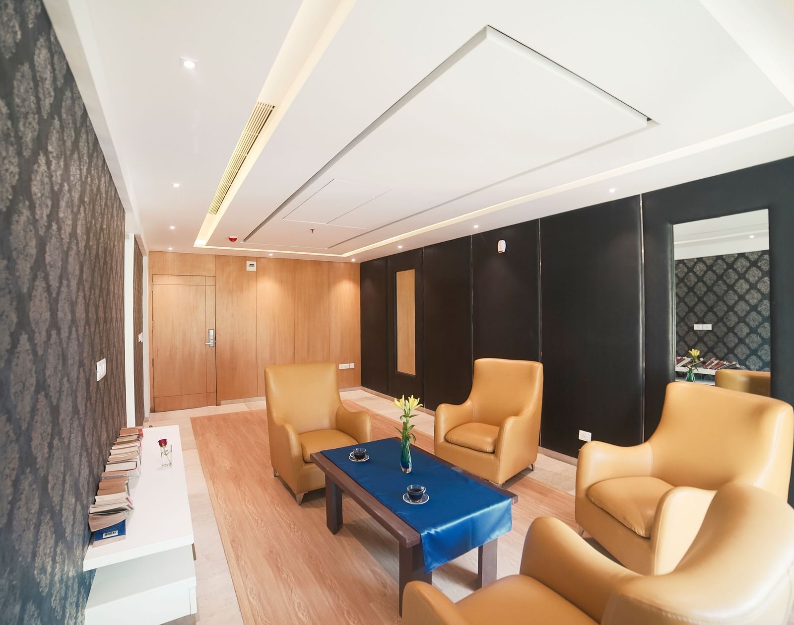 A spacious and inviting lounge area at BNGV Grandeur Hotel and Banquets, with light-colored upholstered chairs, a coffee table, and warm lighting.