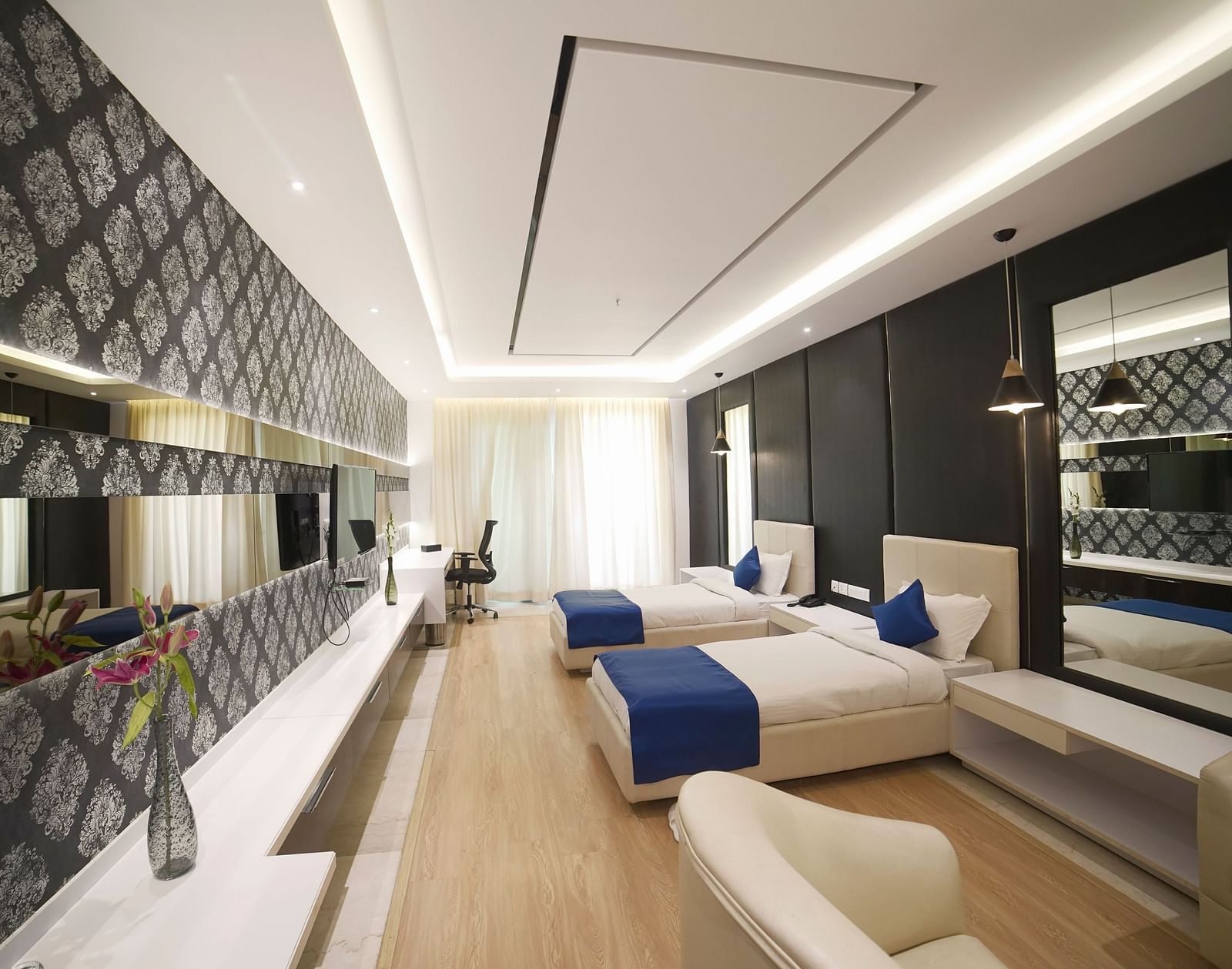  A stylish hotel room at BNGV Grandeur Hotel and Banquets, showcasing a bed with a blue runner, a patterned accent wall, and well-designed lighting.