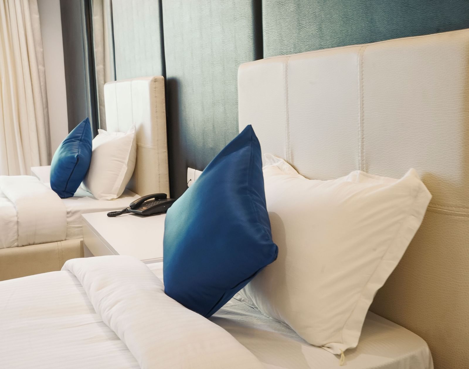 A close-up view of a comfortable bed in a hotel room at BNGV Grandeur Hotel and Banquets, highlighting the soft pillows and blue decorative cushion.