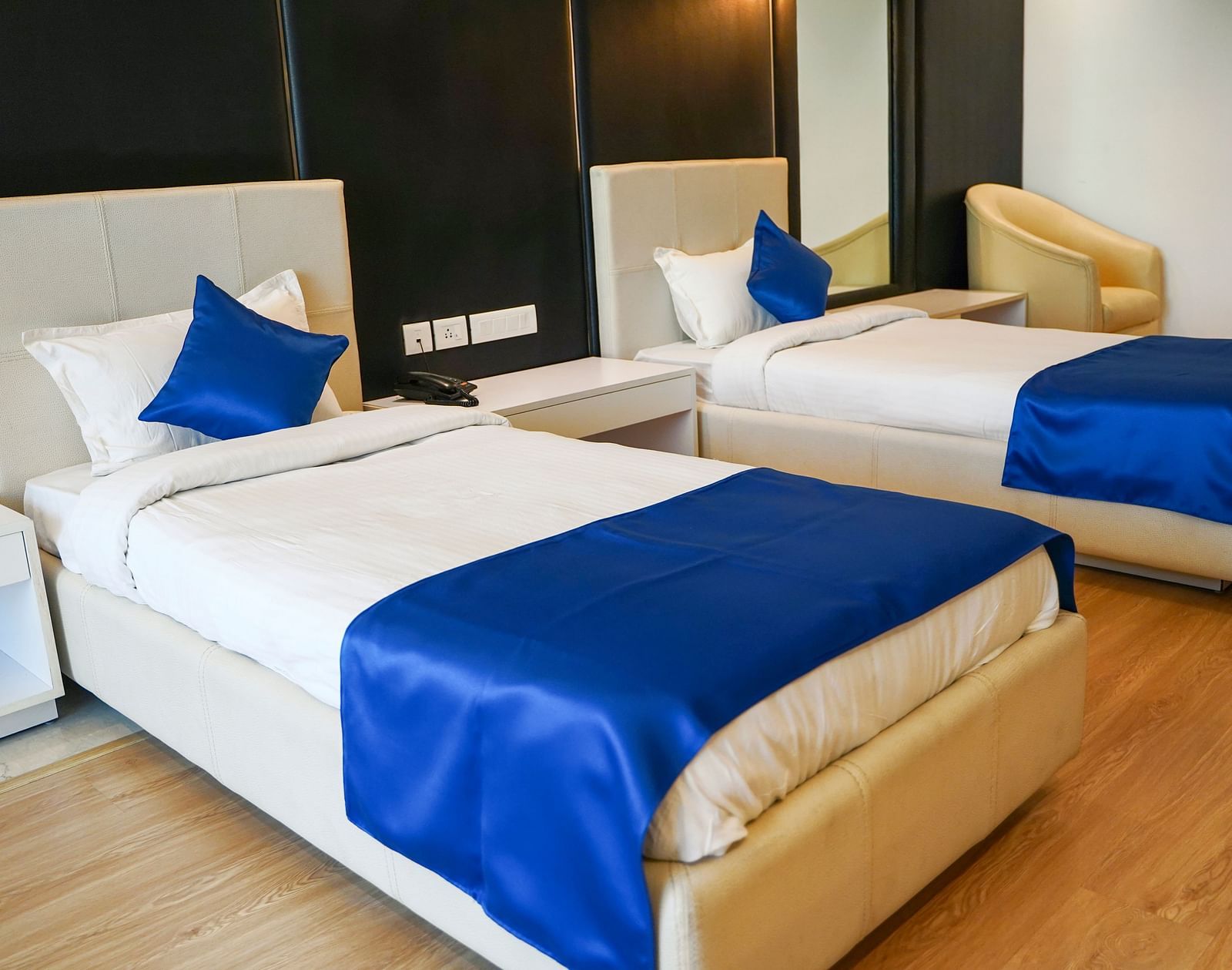 A bright and inviting hotel room at BNGV Grandeur Hotel and Banquets with two beds, each adorned with crisp white linens and a royal blue bed runner.