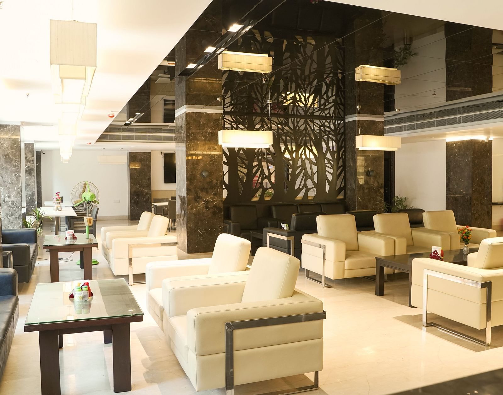 A sophisticated lounge area at BNGV Grandeur Hotel and Banquets with comfortable light-coloured seating, square tables, and a striking reflective ceiling design.